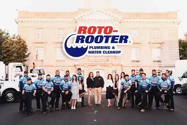 Roto-Rooter team posing in front of a grand building with company trucks
