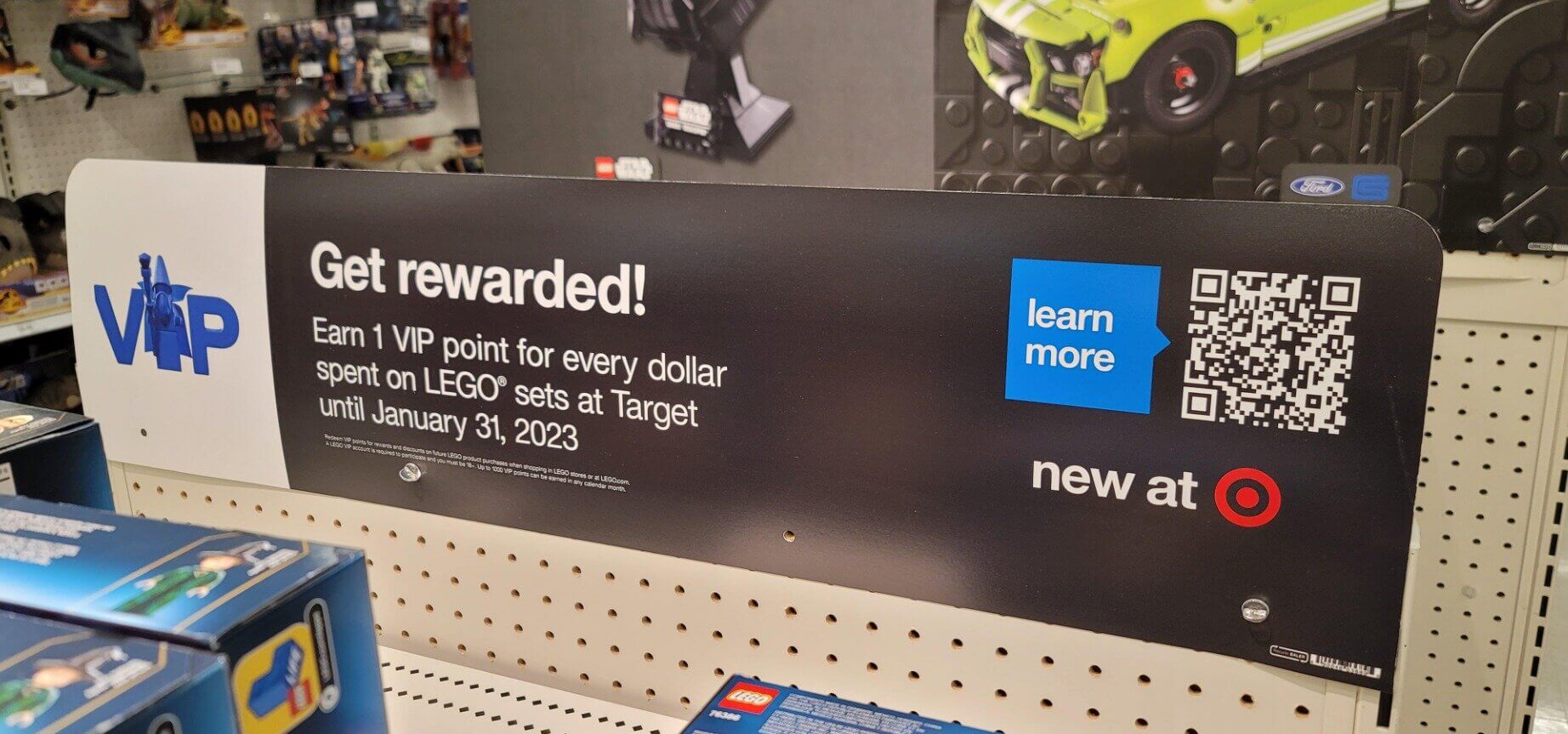 a promotional sign in a retail store advertises a LEGO VIP promotion with a QR code and details of the offer