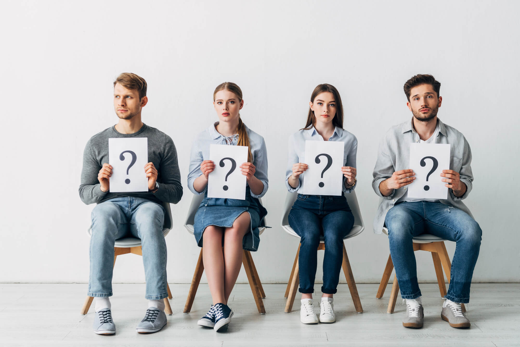 Four young job seekers sitting down, with each holding a question mark sign
