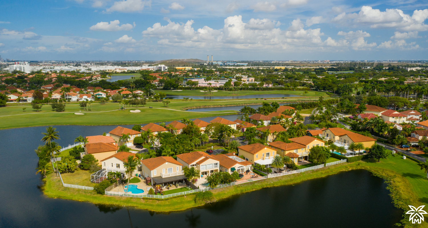 Aerial or street-level view of a picturesque Sarasota neighborhood with palm trees, modern homes, and a sunny sky.