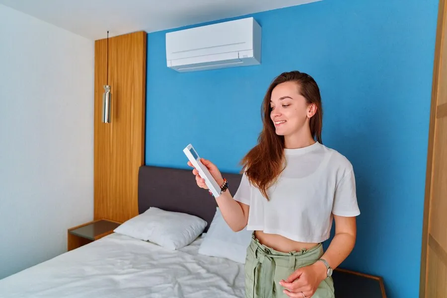 A woman showing a remote controller with a ductless AC at the background