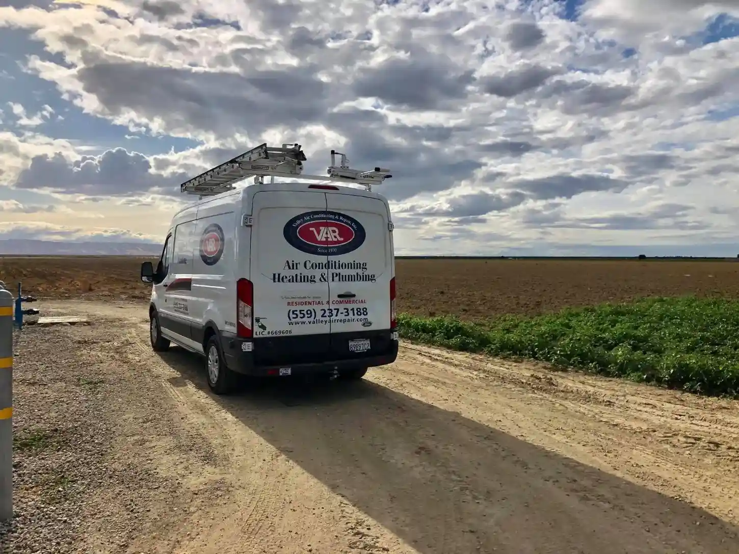 One van is photographed on a dusty dirt road in a field under a dramatic sky, suggesting they serve rural or agricultural locations, as well as typical urban settings