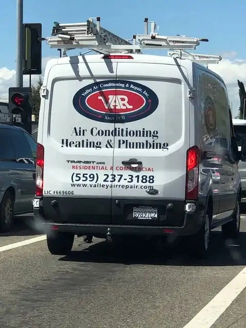 Back of a white Valley Air Conditioning Heating & Plumbing service van on the road with license number and contact information.