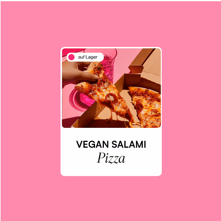 Hand nimmt ein Stück vegane Salami-Pizza aus einer Pizzaschachtel mit einem rosa Hintergrund.