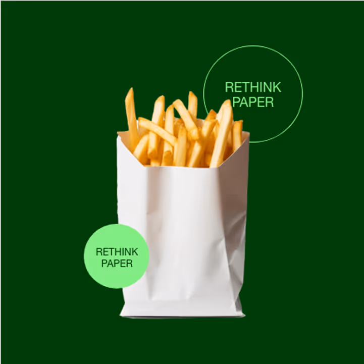Pommes Frites in einer weißen Papiertüte vor grünem Hintergrund mit dem Text „RETHINK PAPER“ in zwei Kreisen.