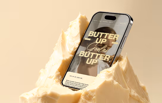 Smartphone mit geöffneter Webseite 'Butter Up' steckend in einem großen Stück Butter.