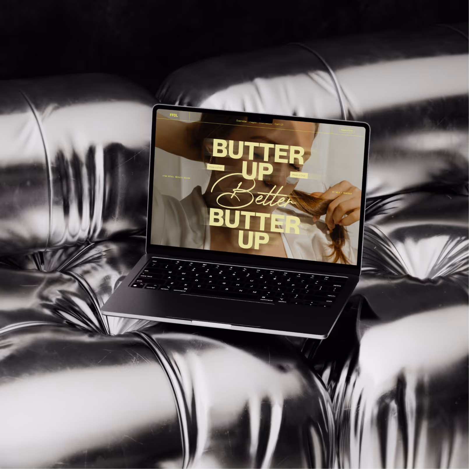 Laptop mit Website-Anzeige 'Butter Up Better Butter Up' auf metallisch glänzendem Sofa.