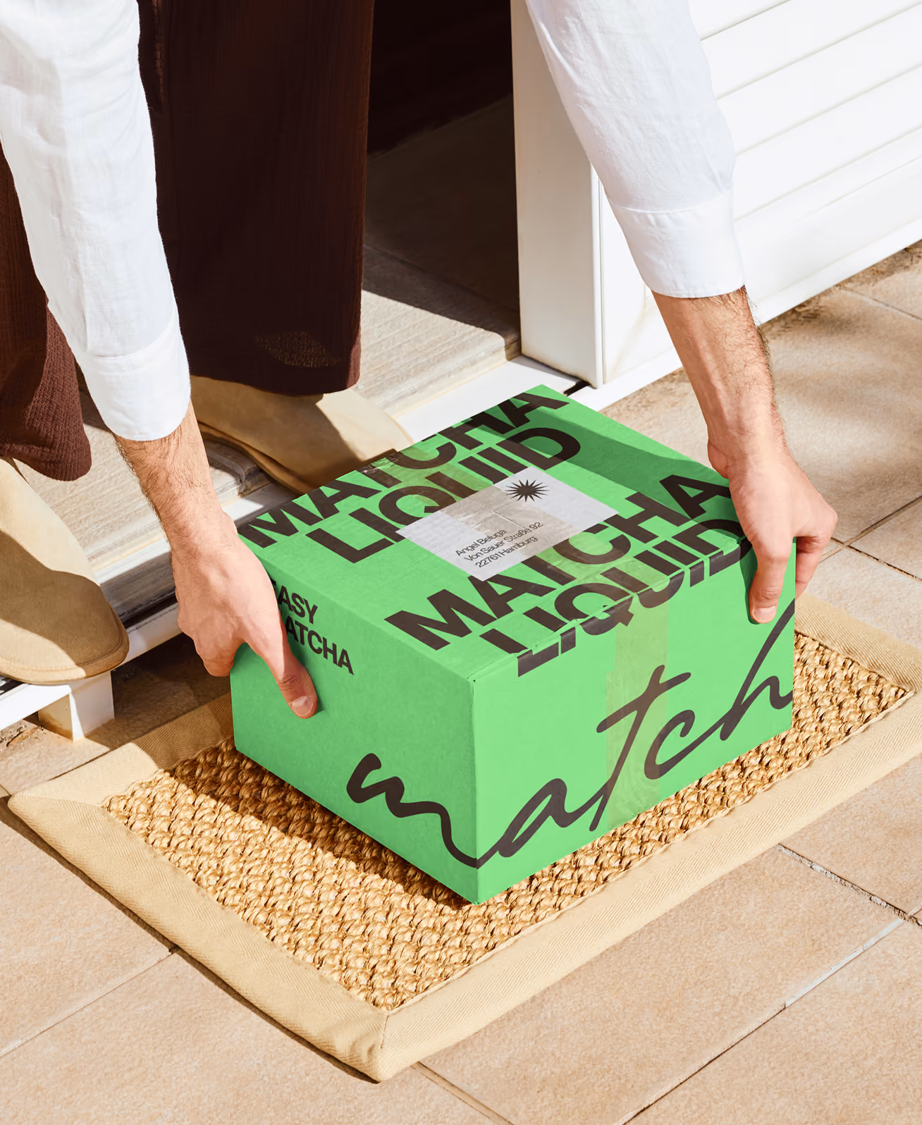 Person stellt grüne Matcha Liquid Verpackung auf einen Teppich vor einer Tür.