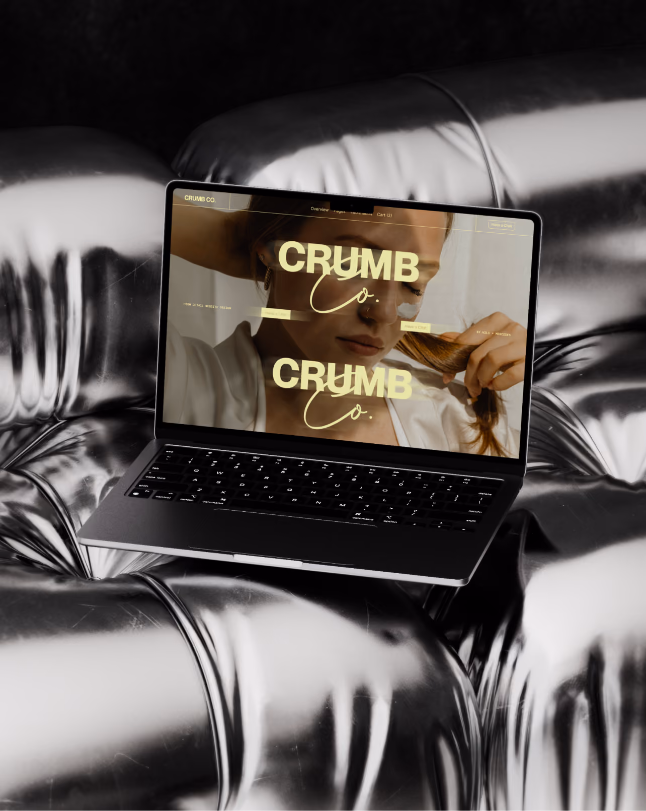 Laptop mit Website-Anzeige 'Butter Up Better Butter Up' auf metallisch glänzendem Sofa.