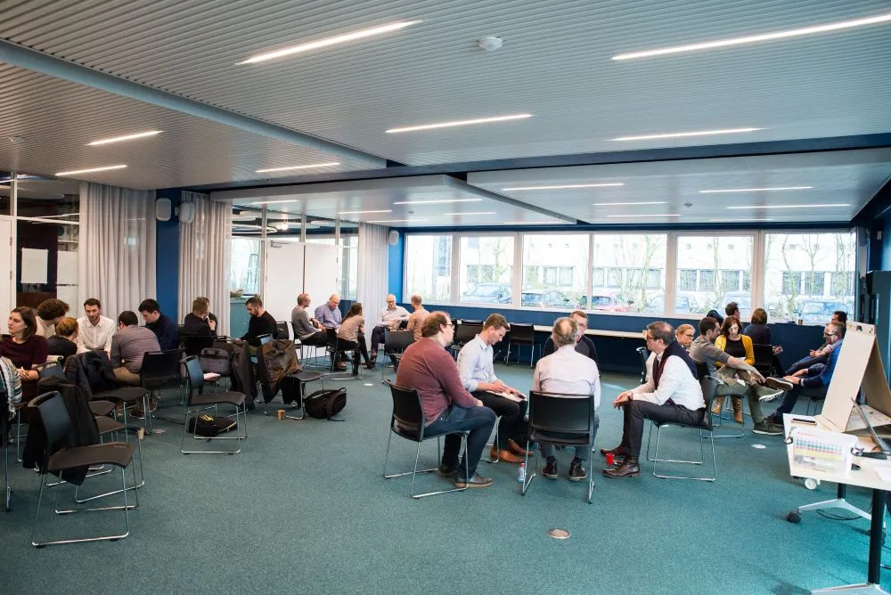 Kleine groepen deelnemers in gesprek tijdens interactieve netwerksessie in vergaderruimte