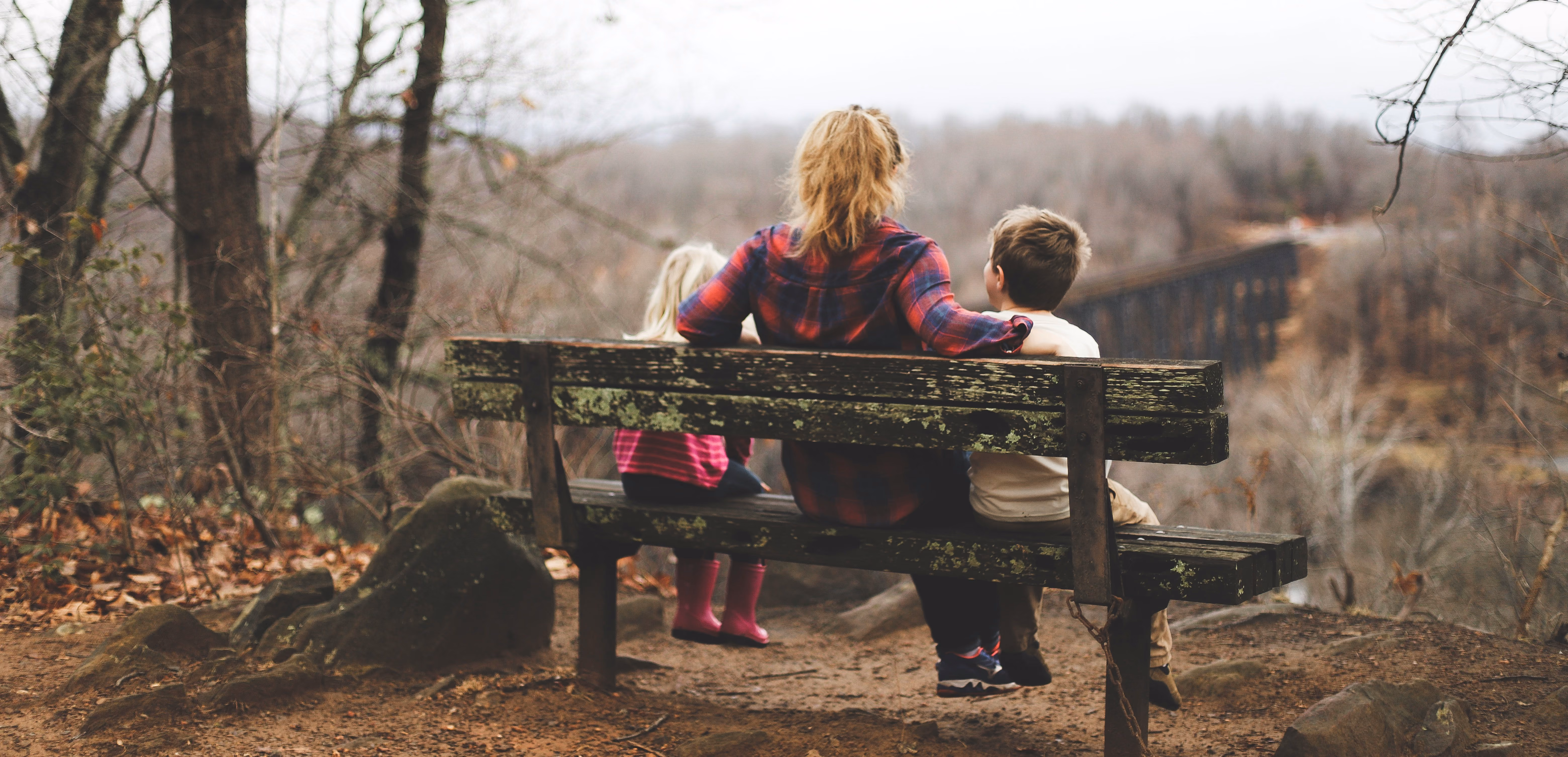 A mother sitting on a bench with her two children