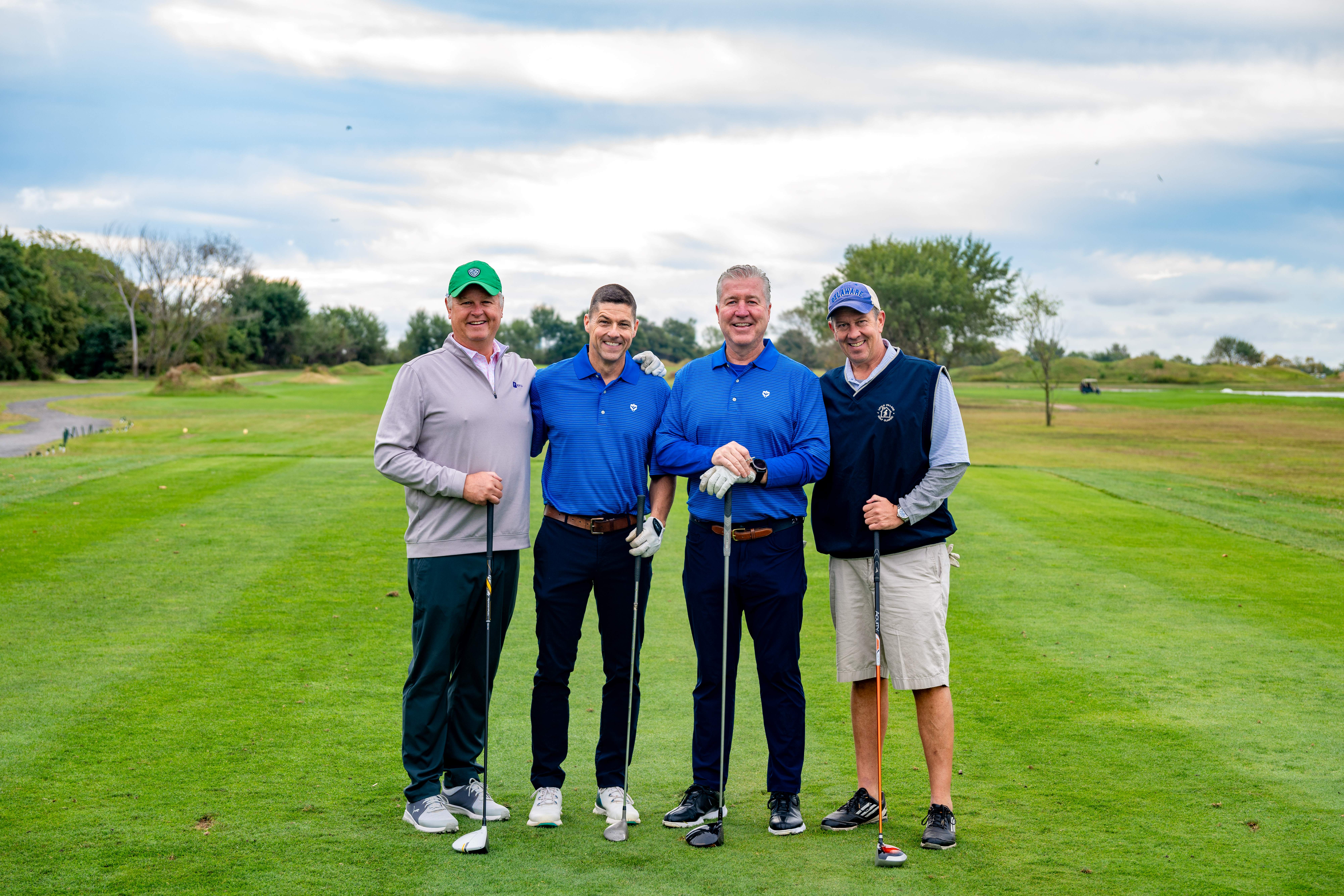 Four males posing with golf clubs on golf course.