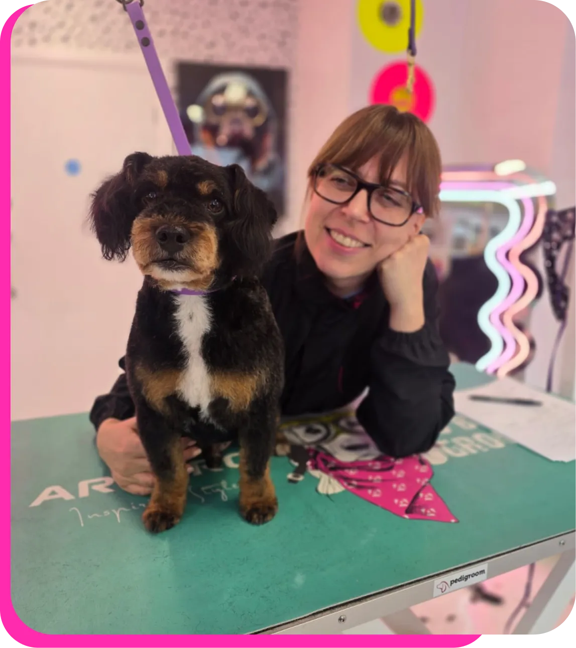 A student on a grooming taster day posing with a small black and tan dog on a grooming table at The Crazy Dog Ladies Grooming Academy salon in St Neots, Cambridgeshire.
