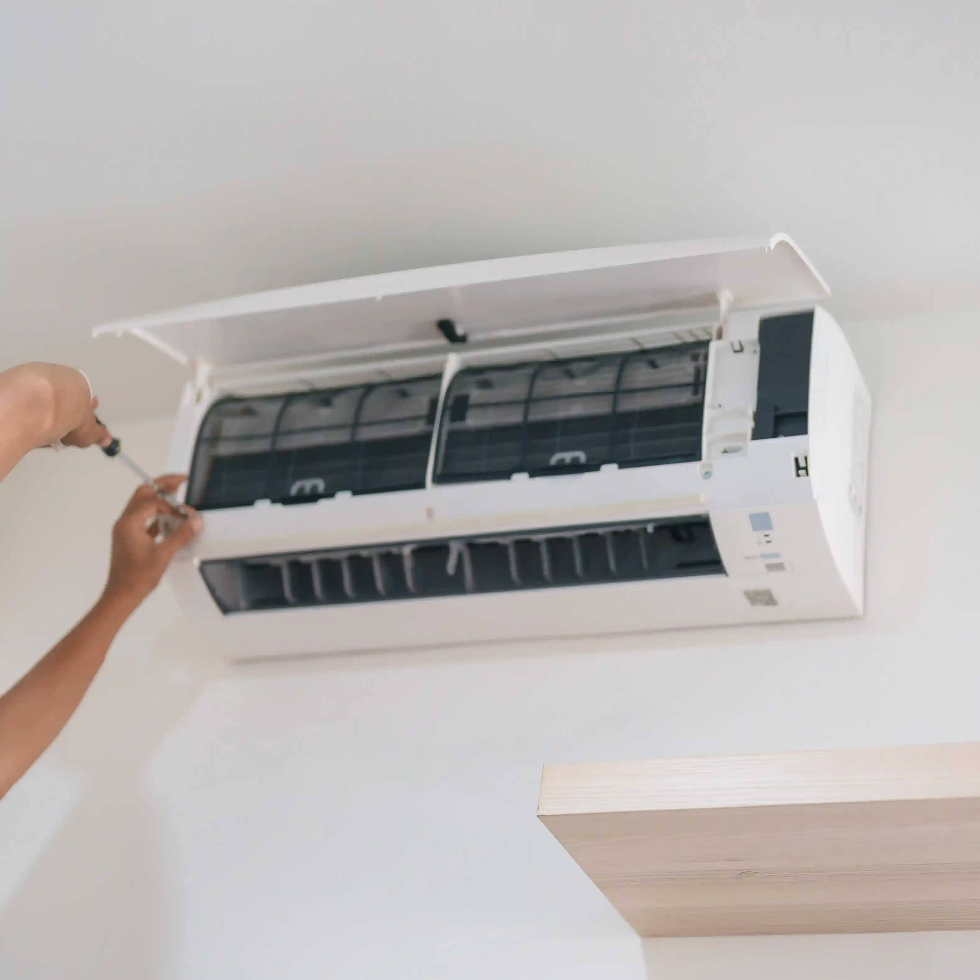 A person's hands are using a screwdriver to work on a wall-mounted air conditioner.