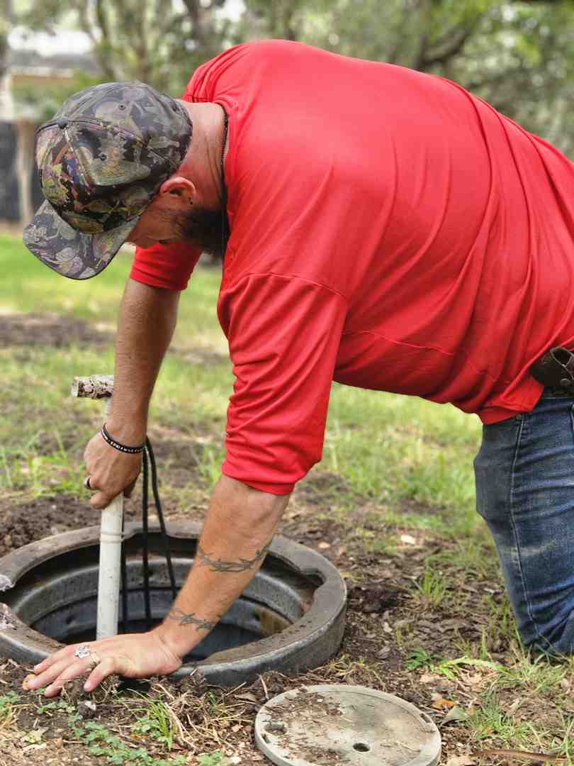 Van Delden technician safely accessing a leach field cleanout port using brand colors #fe0103, #ffffff, #000000 - cleaning leach field lines