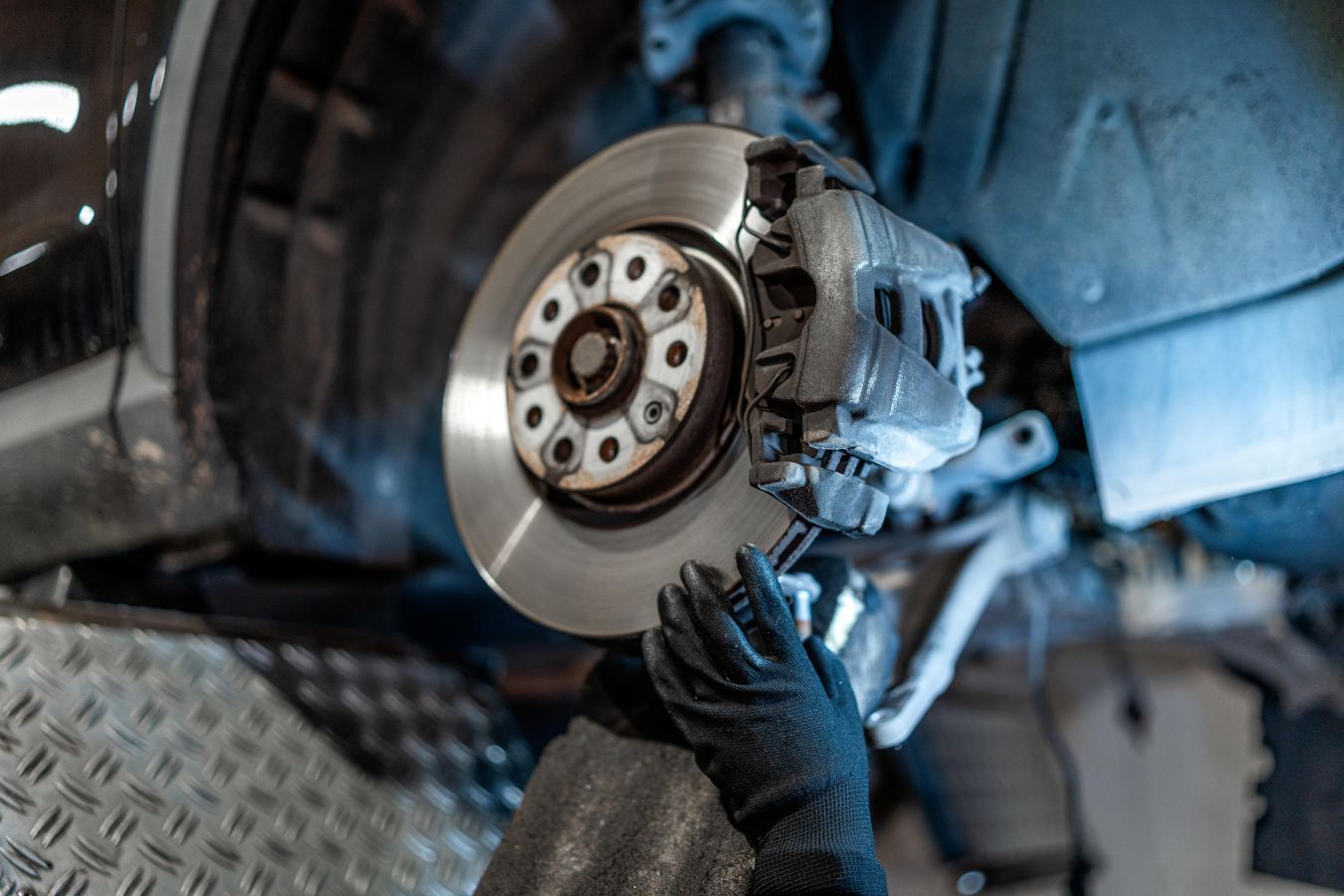 Technician inspecting a brake rotor, caliper and suspension for salt corrosion after an Edmonton winter