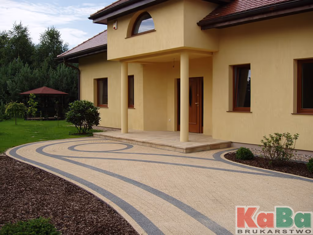 Podjazd i wejście do domu z żółtymi ścianami i dwiema kolumnami, otoczone zielonym ogrodem.