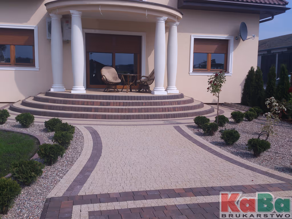 Front domu z okrągłym tarasem z białymi kolumnami, zadaszonym dachem oraz zadbaną ścieżką z kostki brukowej i roślinami.