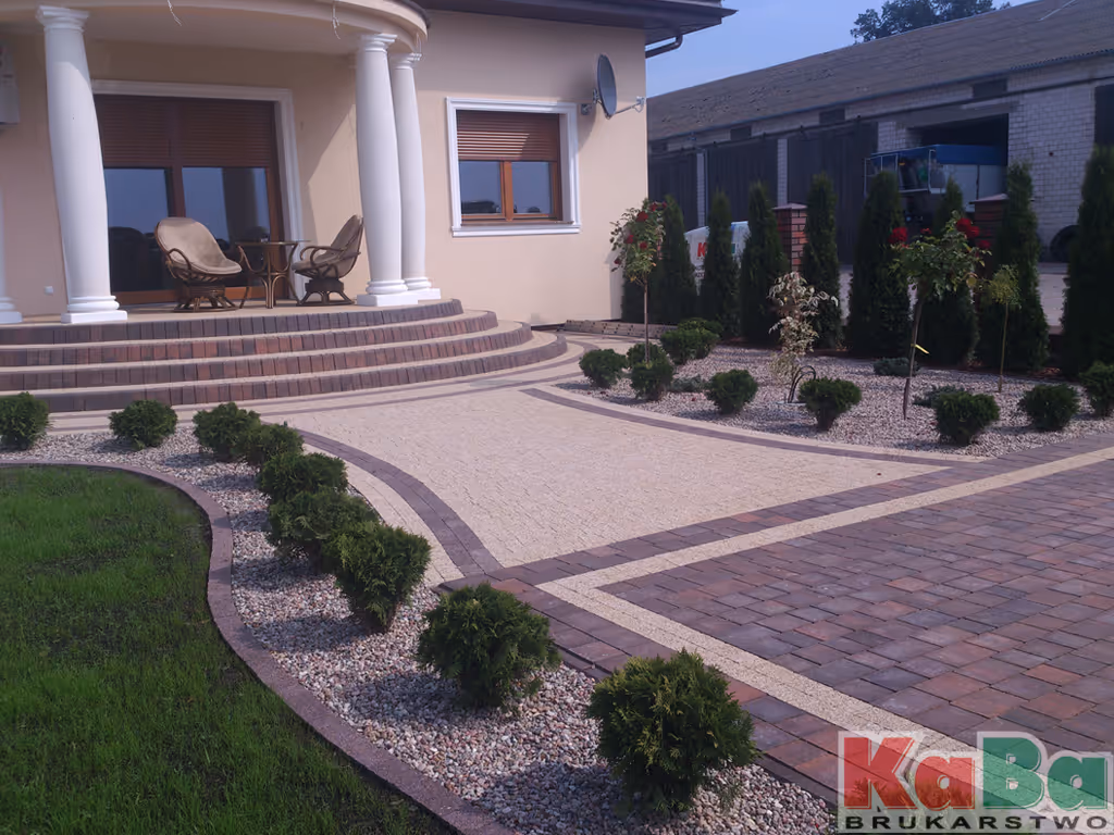 Podwórko z elegancką, kręconą ścieżką i niskimi krzewami przy domu z kolumnami i meblami tarasowymi.