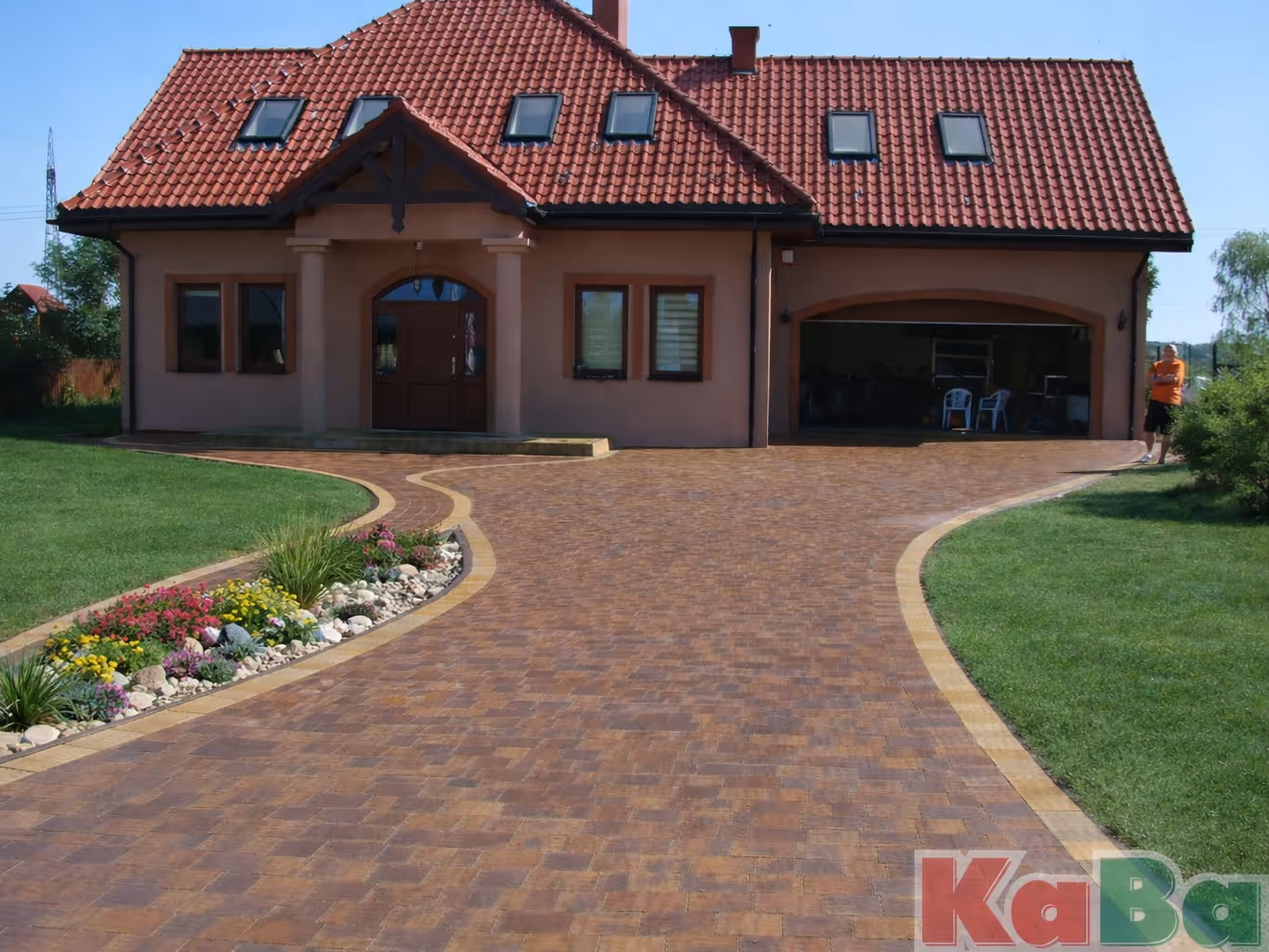 Dom z czerwonym dachem i podjazdem z kostki brukowej z wyodrębnionym pasem ziemi pośrodku.