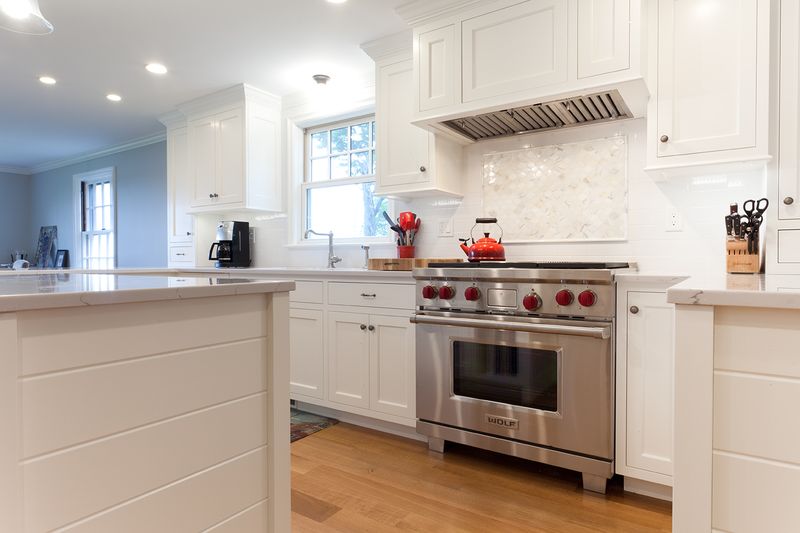 White custom kitchen with a professional range, marble backsplash, and hardwood floors