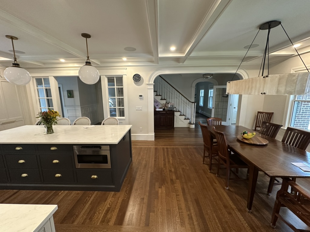 Open kitchen and dining room with a navy island, coffered ceiling, and a long farmhouse table on hardwood floors