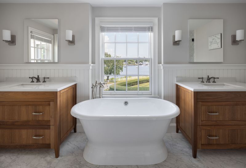 Primary bathroom with a freestanding tub, wood vanities, and a double-hung window with water views