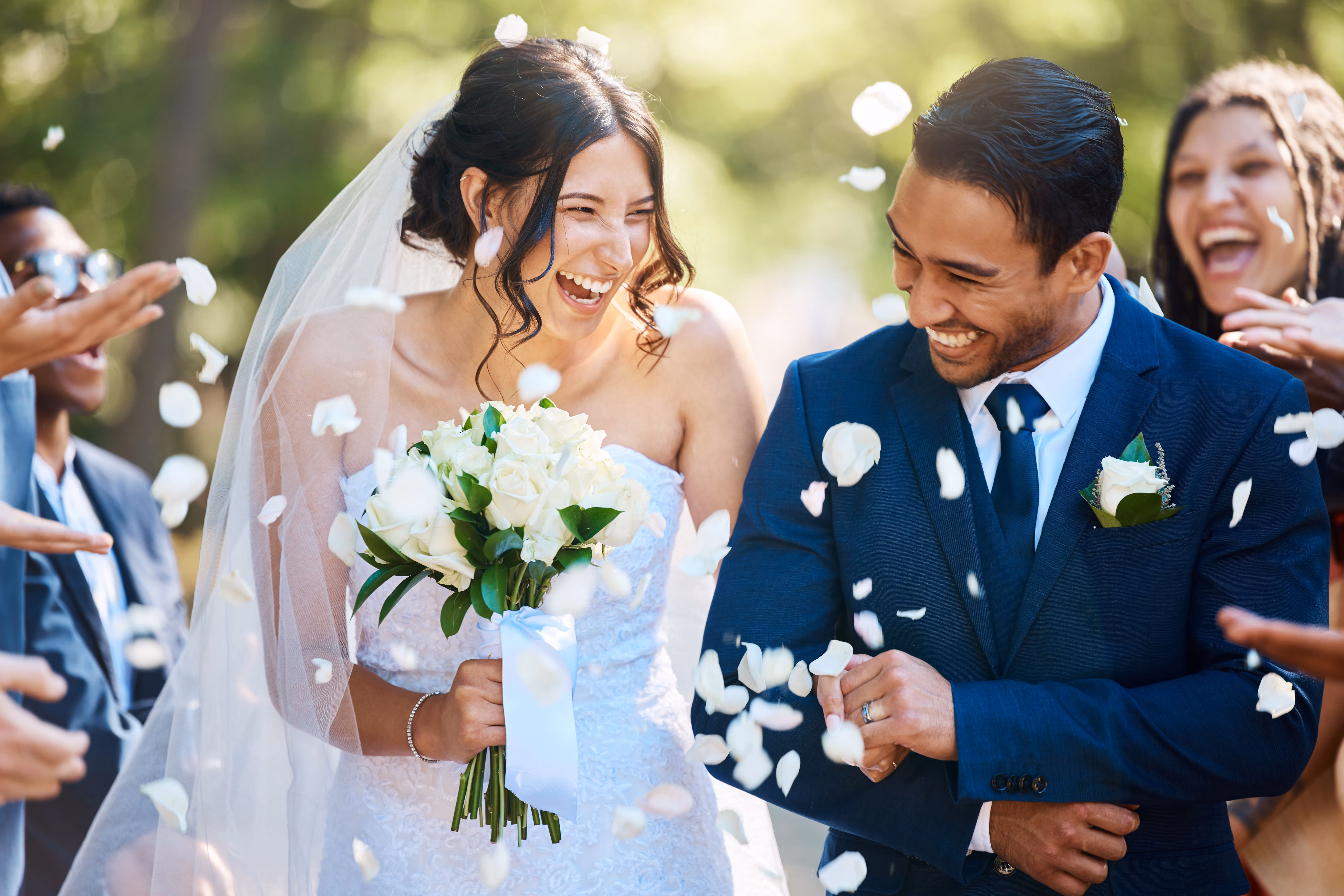 Bride and groom laughing joyfully as white rose petals are thrown around them during their wedding.