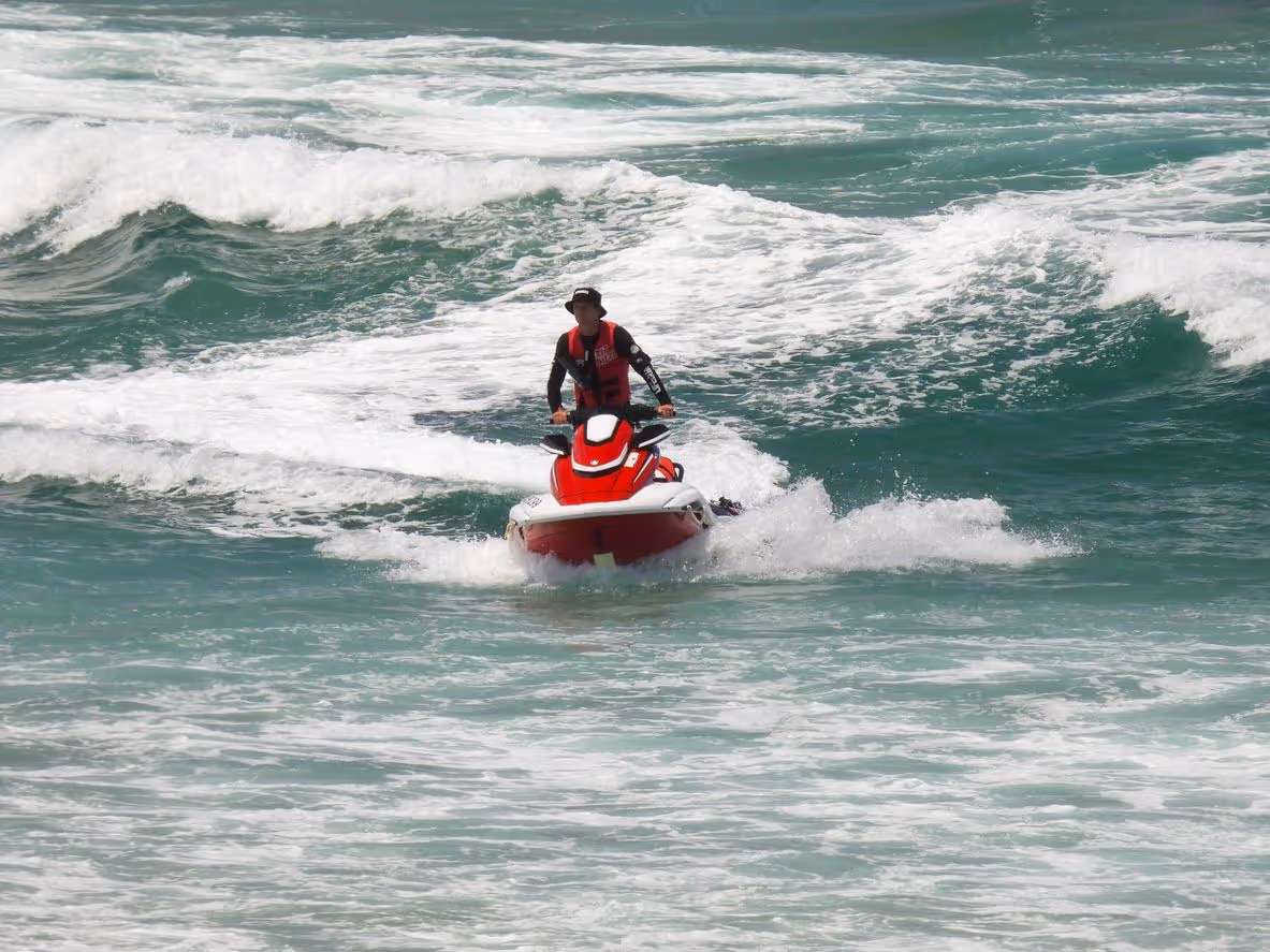 Man riding a red and white jet ski in choppy ocean waves.