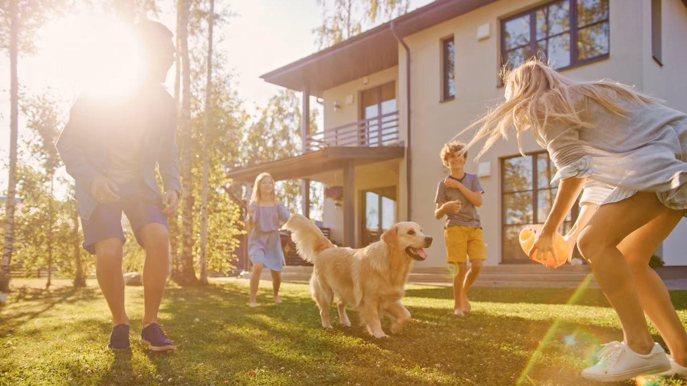 A family with children and a golden retriever playing on a sunny lawn in front of a house.