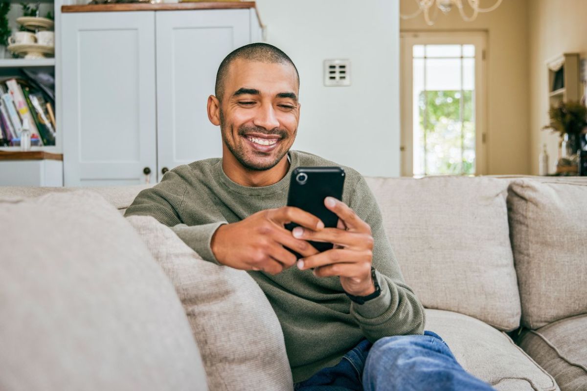 A man smiling while looking at his phone while relaxing on a couch