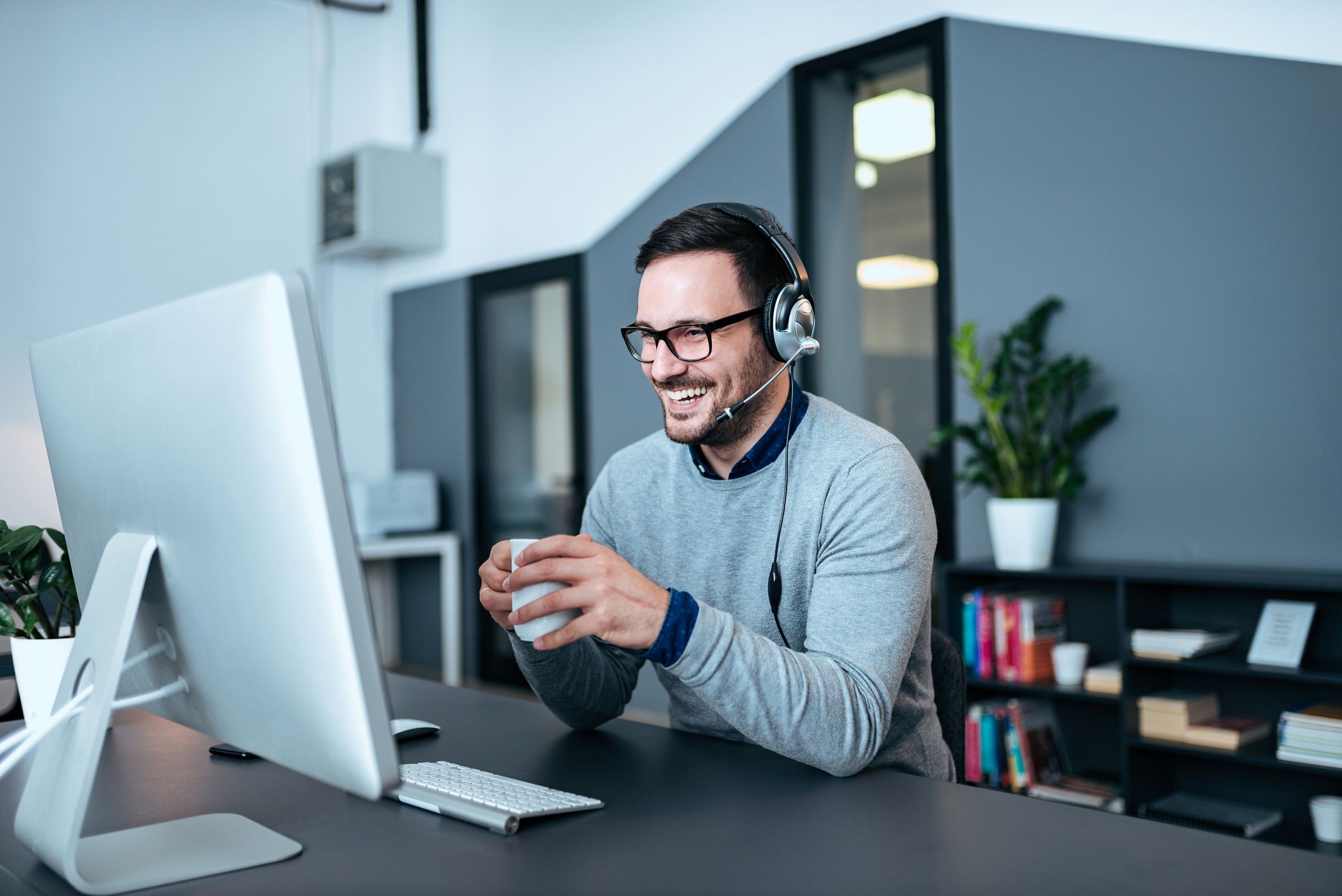Man wearing a headset smiling while using a desktop computer in an office