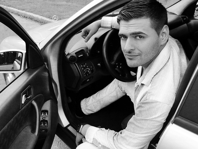 Homme assis dans le siège du conducteur d'une voiture, regardant vers la caméra avec une légère expression souriante.