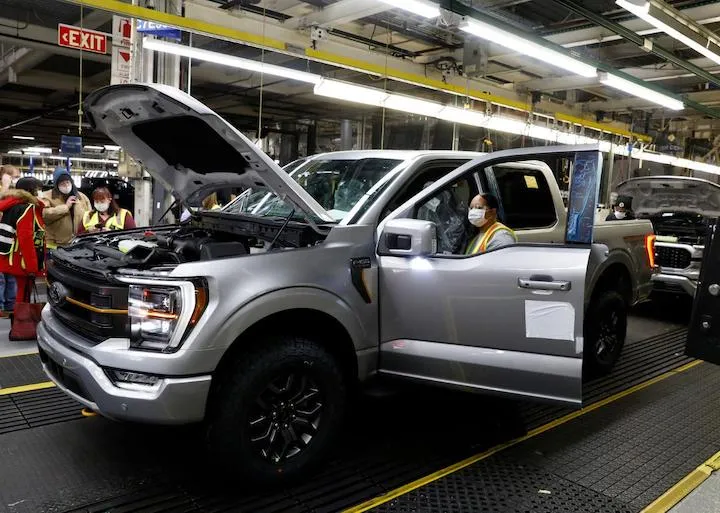 Silver Ford F-150 pickup truck on assembly line with workers in background