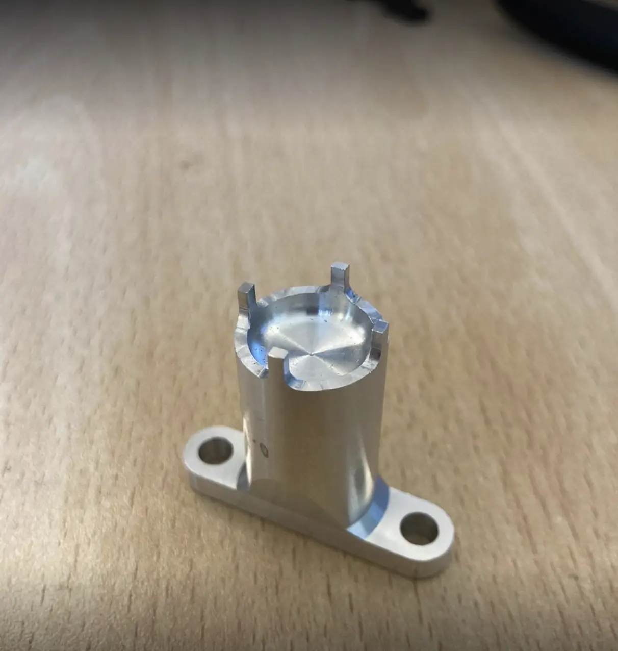 Cylindrical machined aluminum part with a flanged base and top notches, designed for precise mounting or alignment applications.