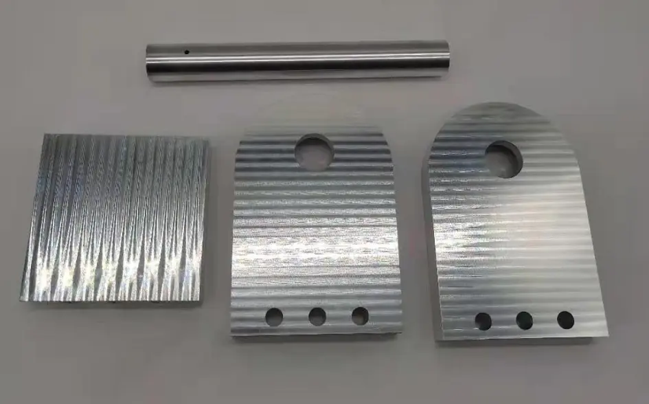 Set of CNC-machined aluminum components including flat plates and a cylindrical rod, all with precision-cut features.