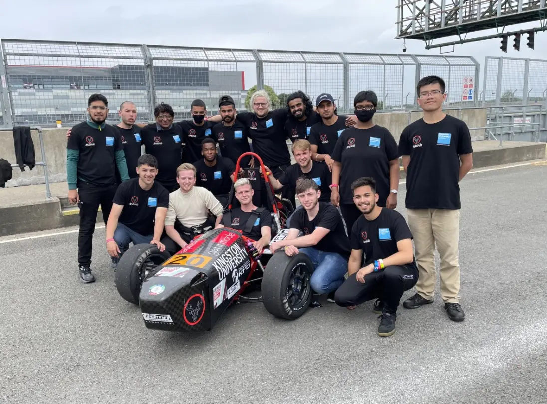 Kingston University Formula Student team posing with their custom-built race car on the track.