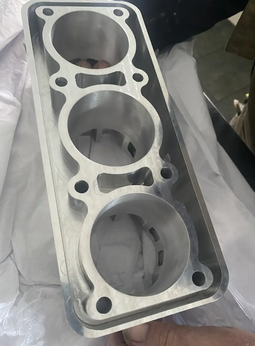 Precision CNC-machined aluminum cylinder block featuring three large bores and bolt holes, held for inspection.