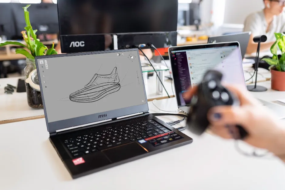 A person holding a game controller in front of a laptop
