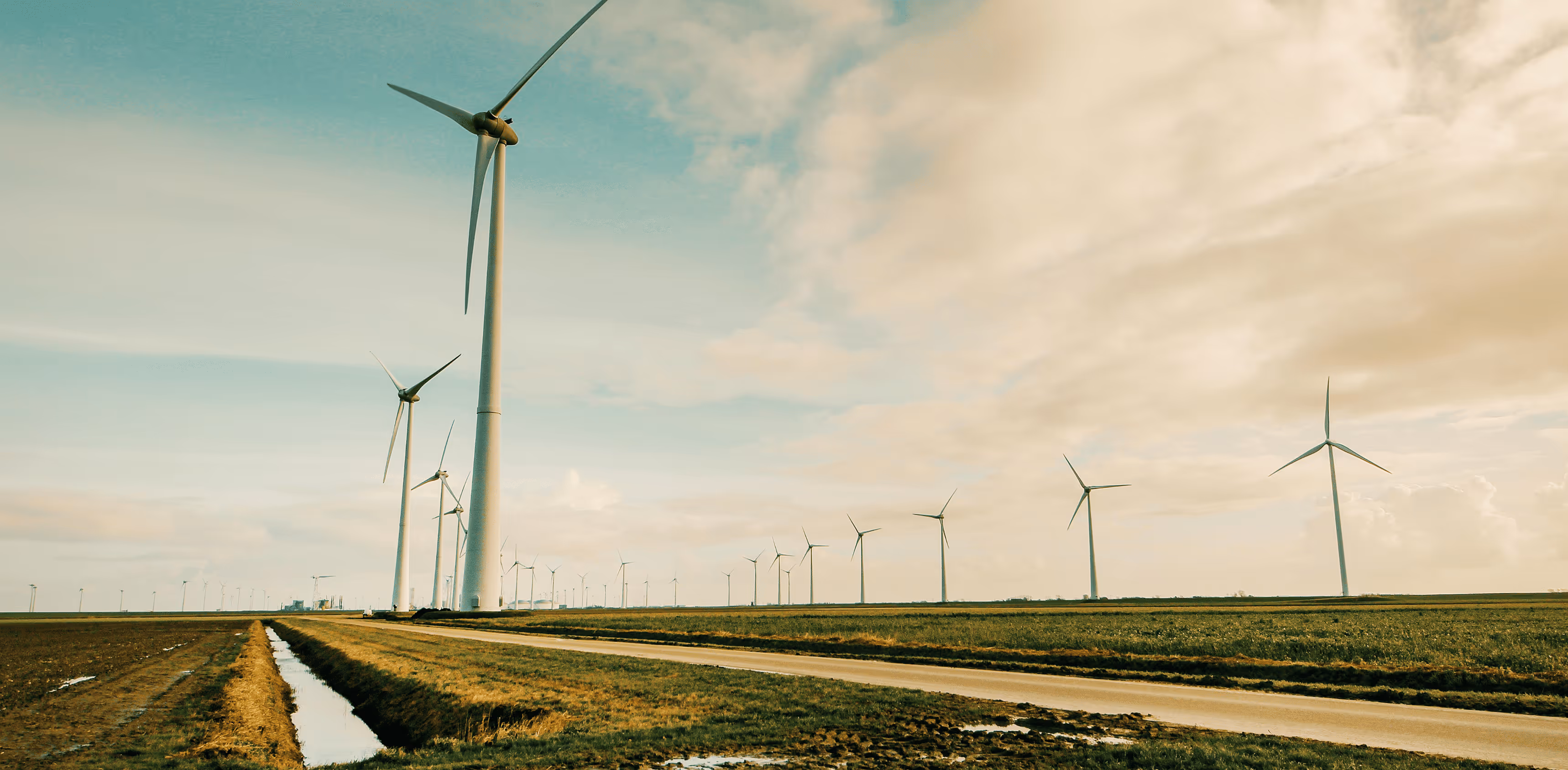 A wind turbine stands tall in a grassy field under a partly cloudy sky, surrounded by other turbines in a wind farm.