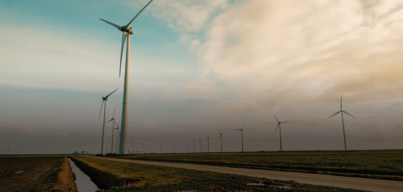 A wind turbine stands tall in a grassy field under a partly cloudy sky, surrounded by other turbines in a wind farm.