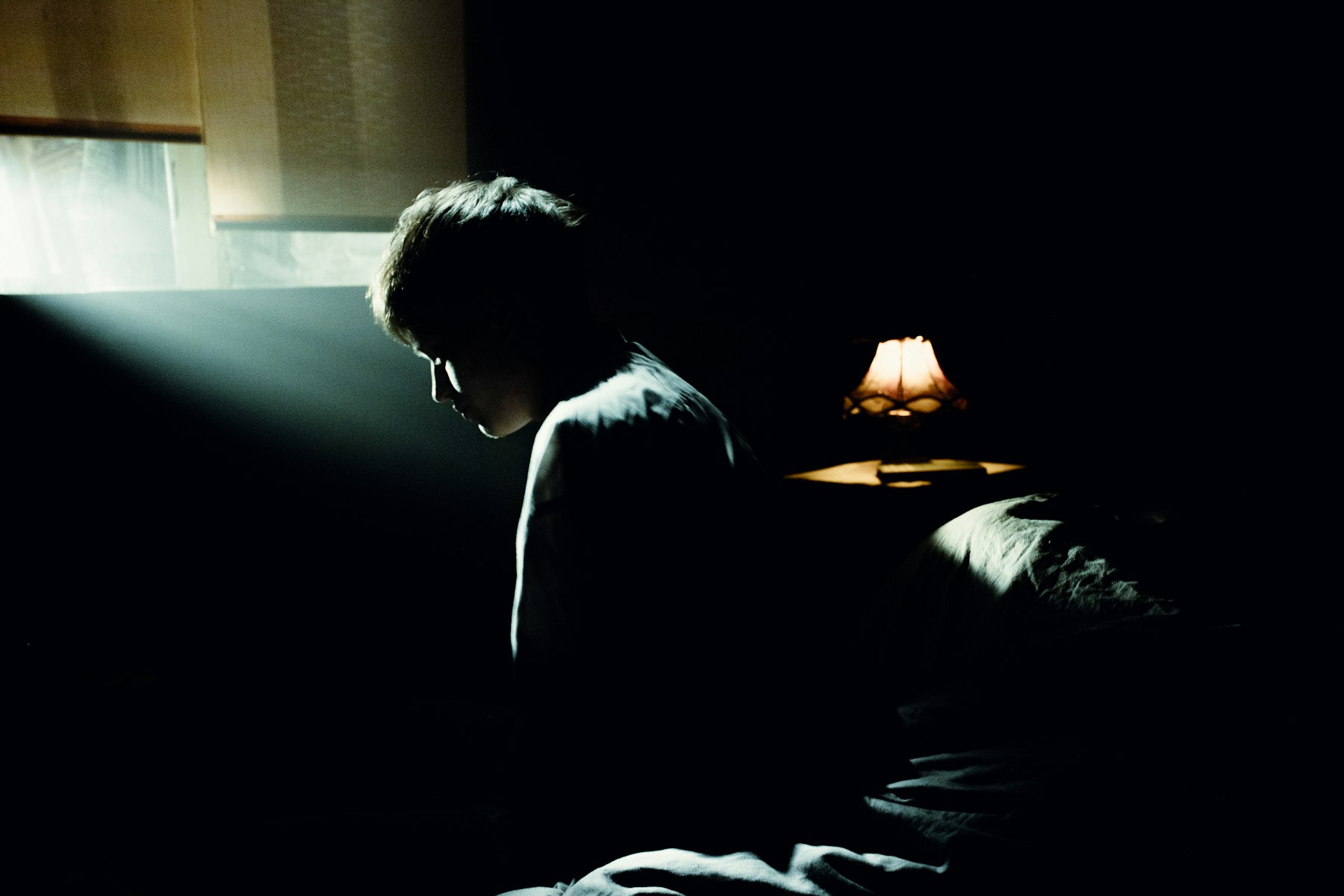 Person sitting awake on the edge of a bed at night
