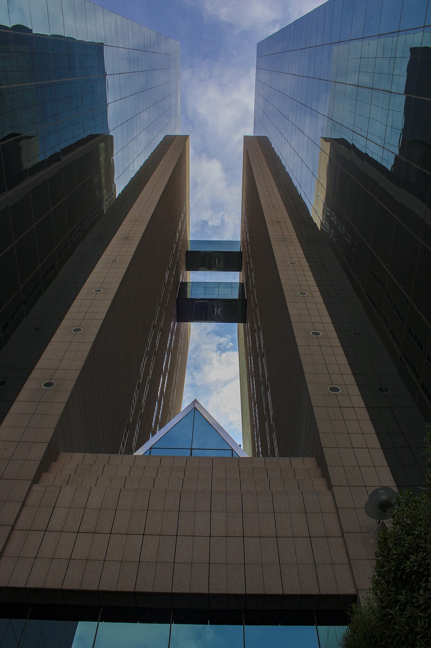 A tall, brown building with a gap between to towers.  There are two enclosed bridges connecting the two towers.  The photo is pointed up from street level.
