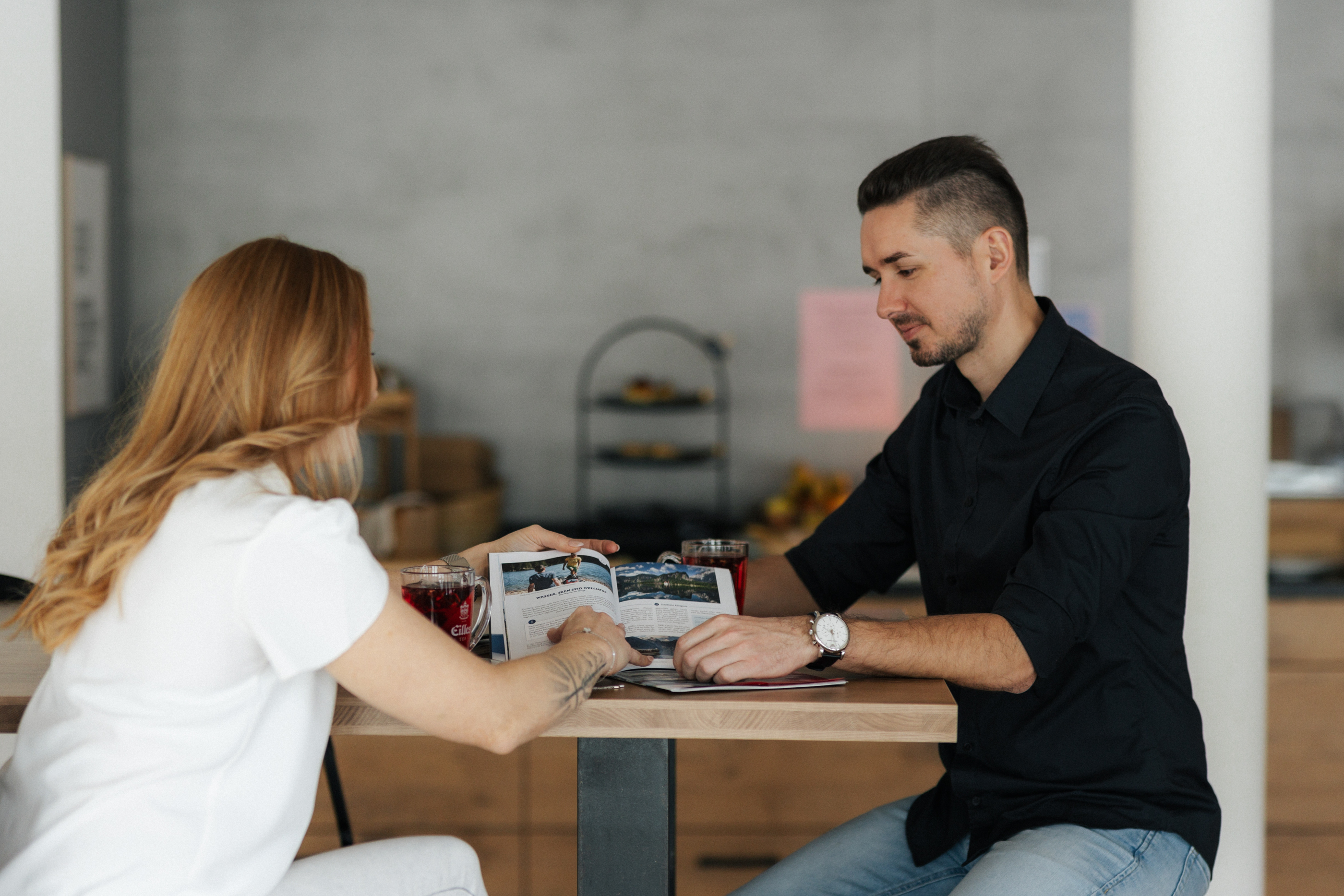 Ein Mann und eine Frau sitzen an einem Holztisch und schauen gemeinsam in eine Broschüre.