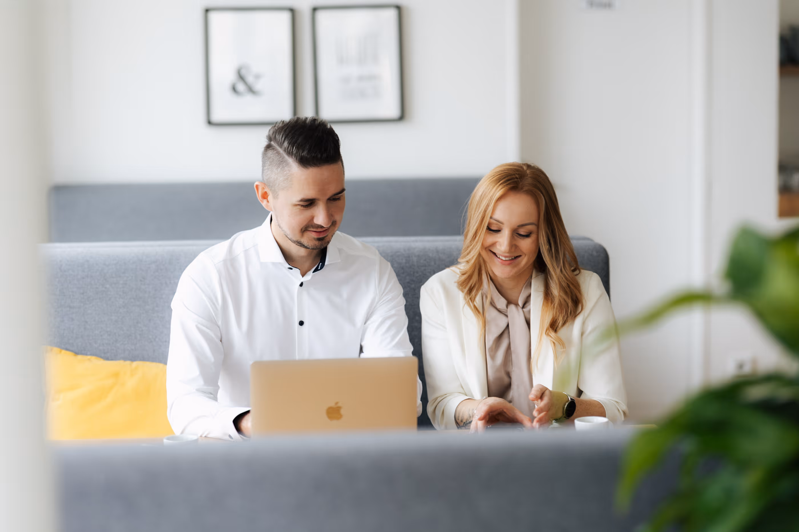 Zwei Personen sitzen in einem modernen Büro an einem Laptop, lächelnd und im Gespräch.