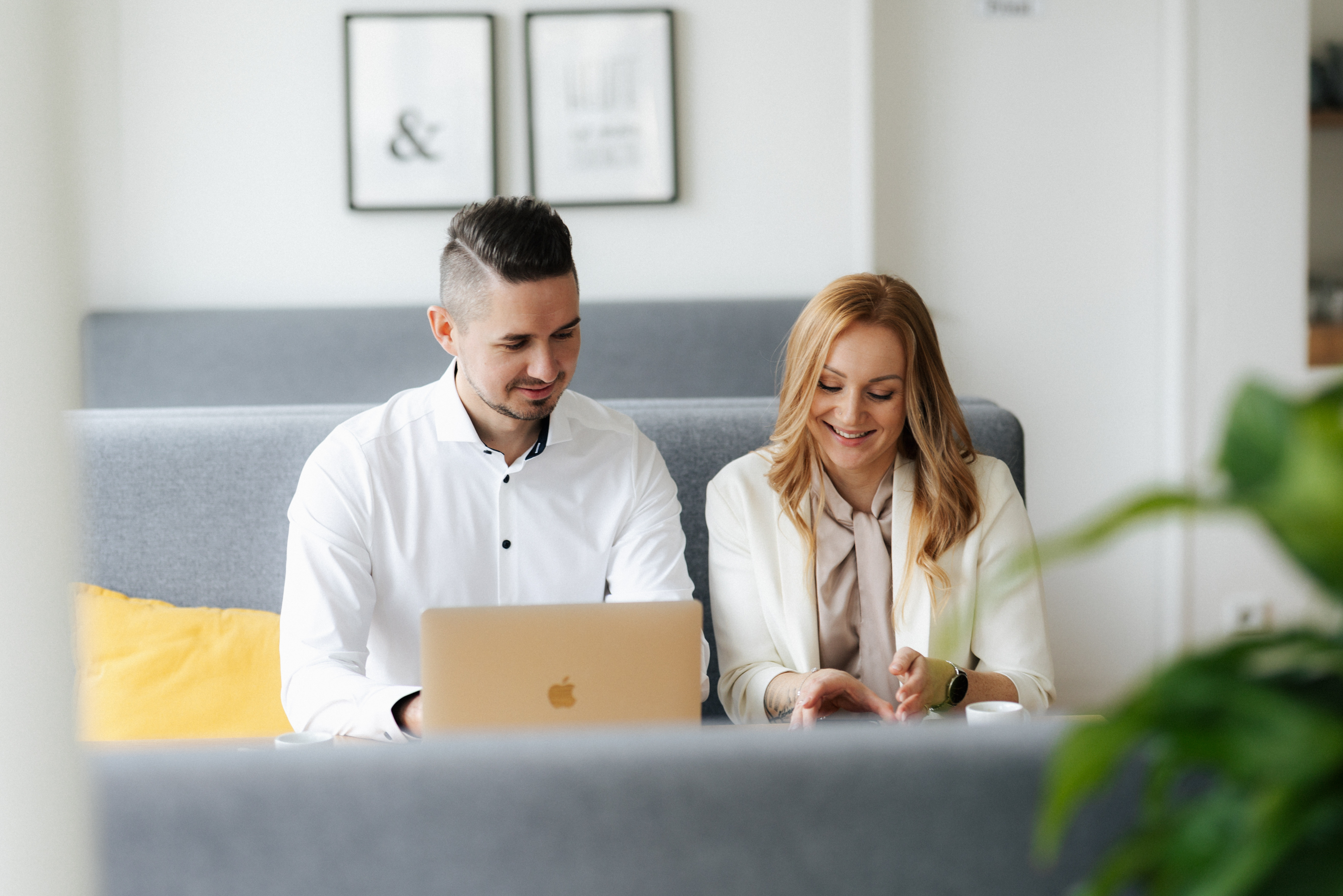 Zwei Personen sitzen in einem modernen Büro an einem Laptop, lächelnd und im Gespräch.