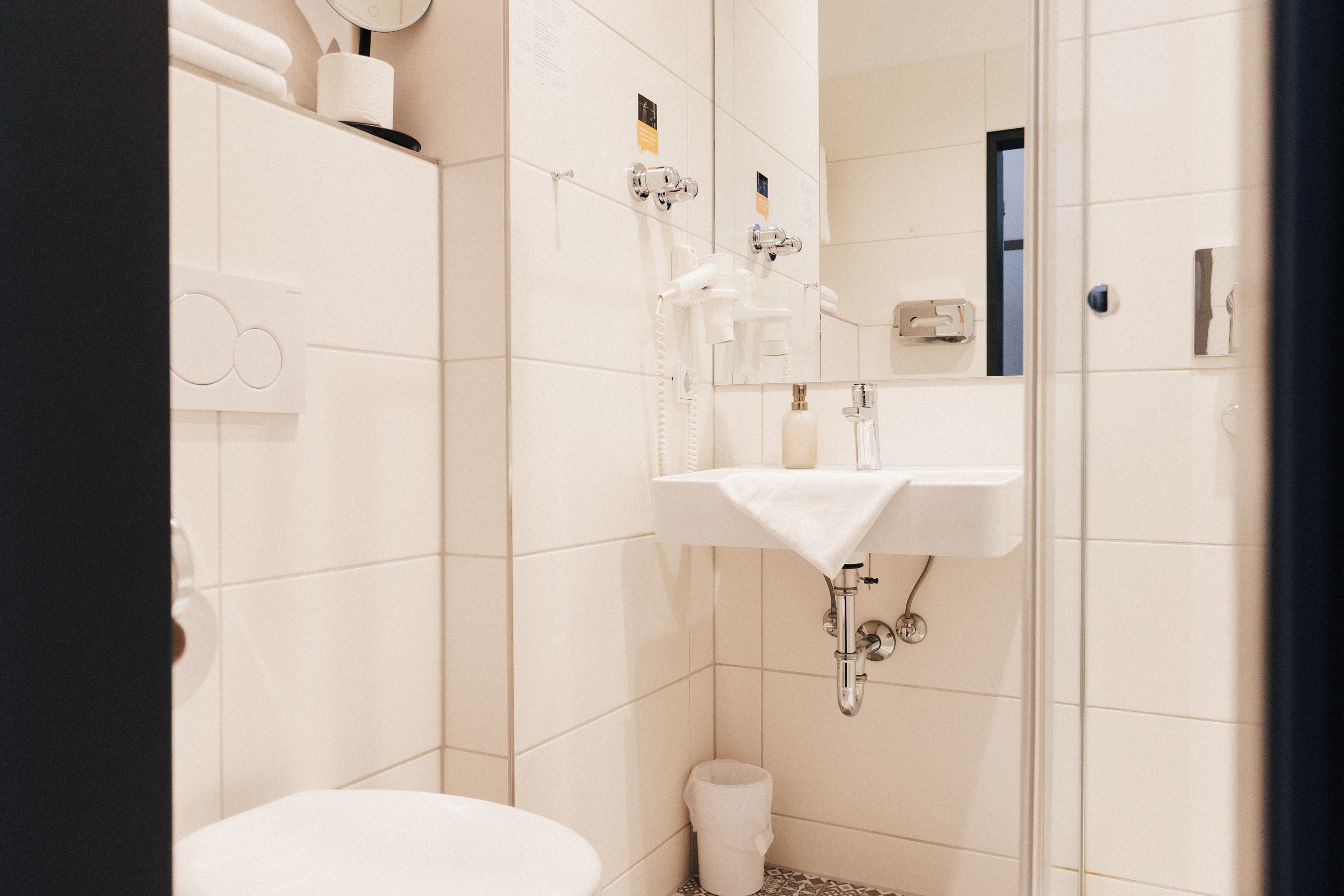 Kleines modernes Badezimmer mit weißem Waschbecken, Handtuch, Spiegelfön und WC.