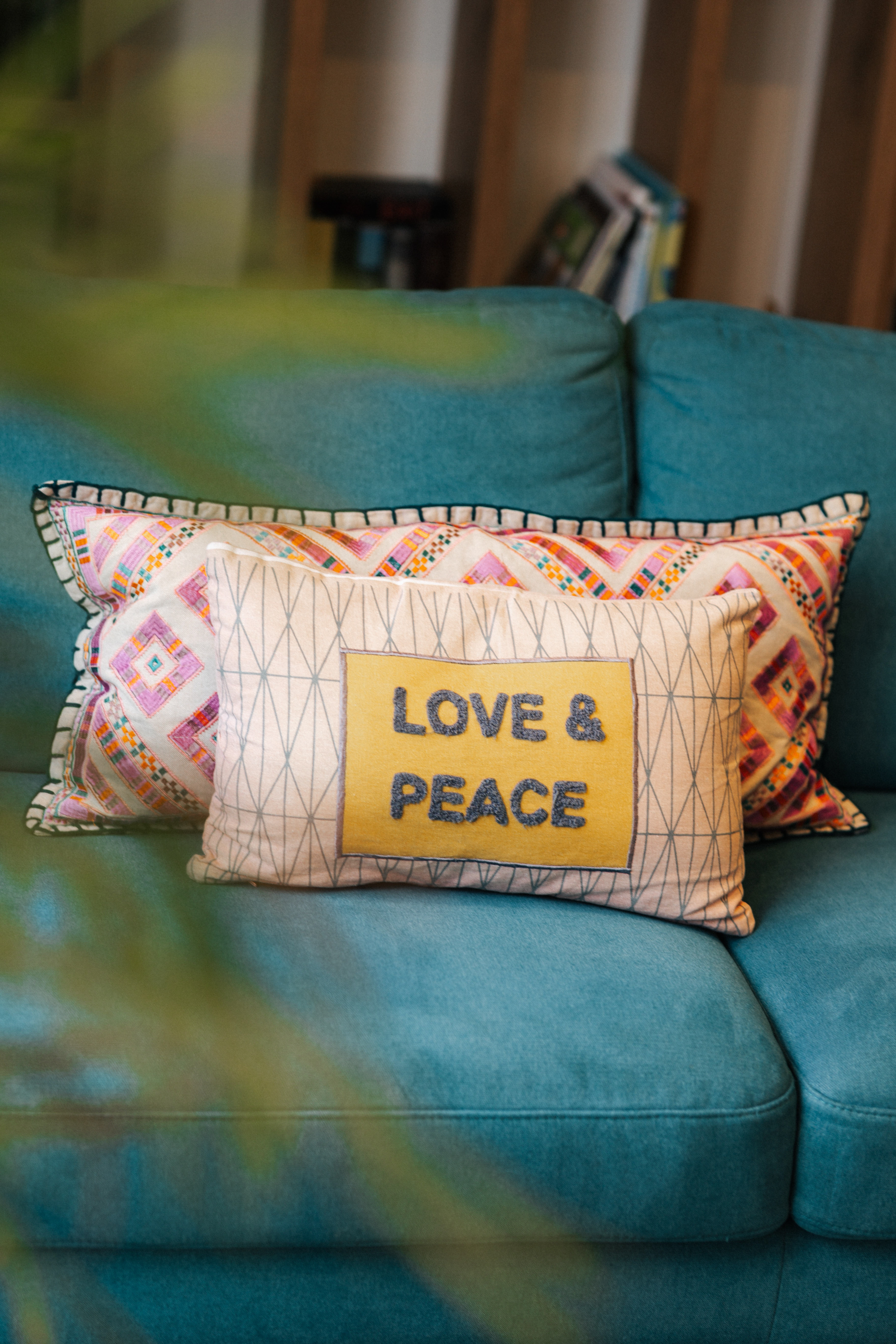 Zwei dekorative Kissen auf einem türkisfarbenen Sofa, eines mit dem Schriftzug 'LOVE & PEACE'.