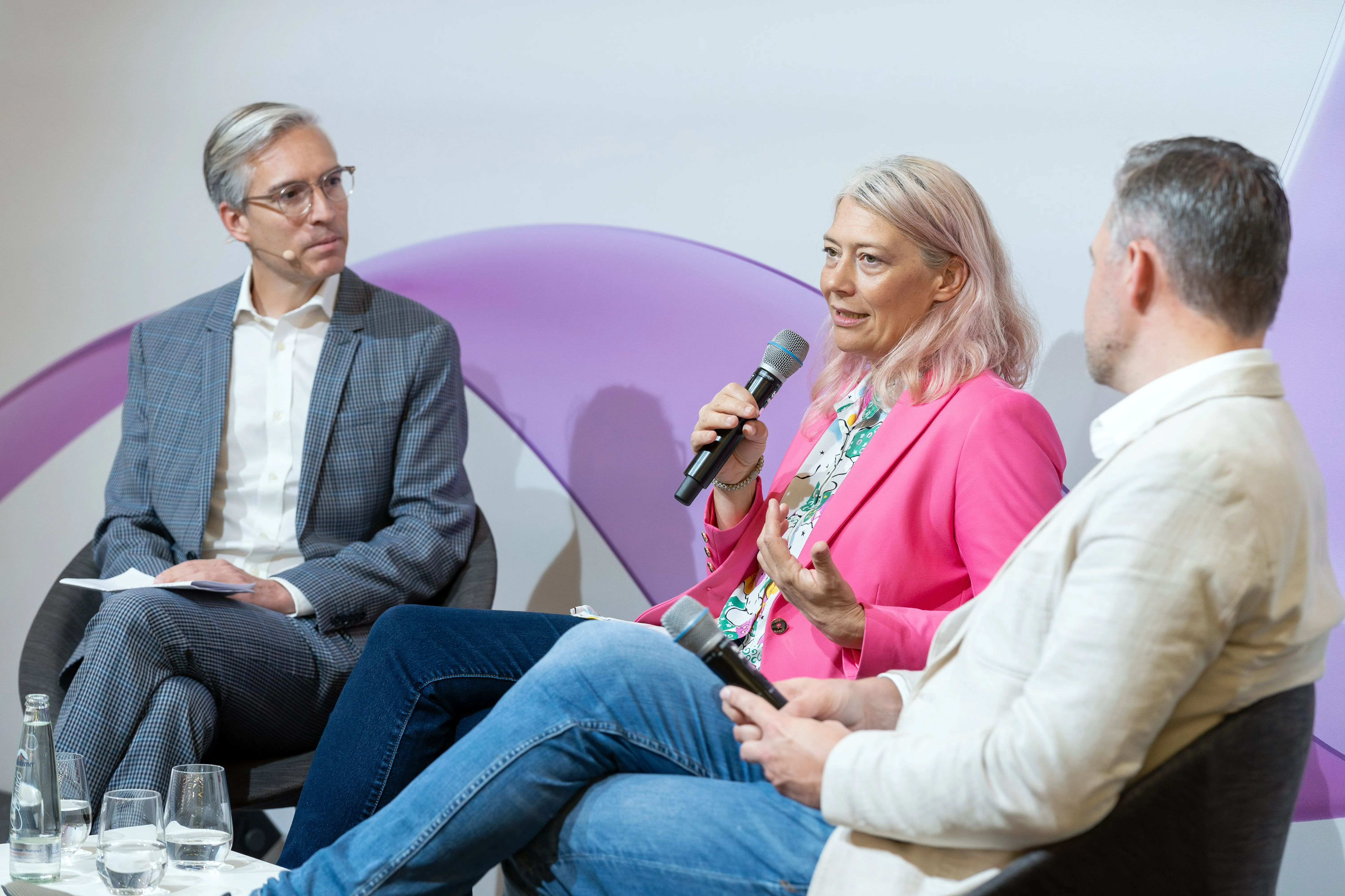 Drei Personen auf der Bühne und Judith Fiedler hat das Mikrofon in der Hand.