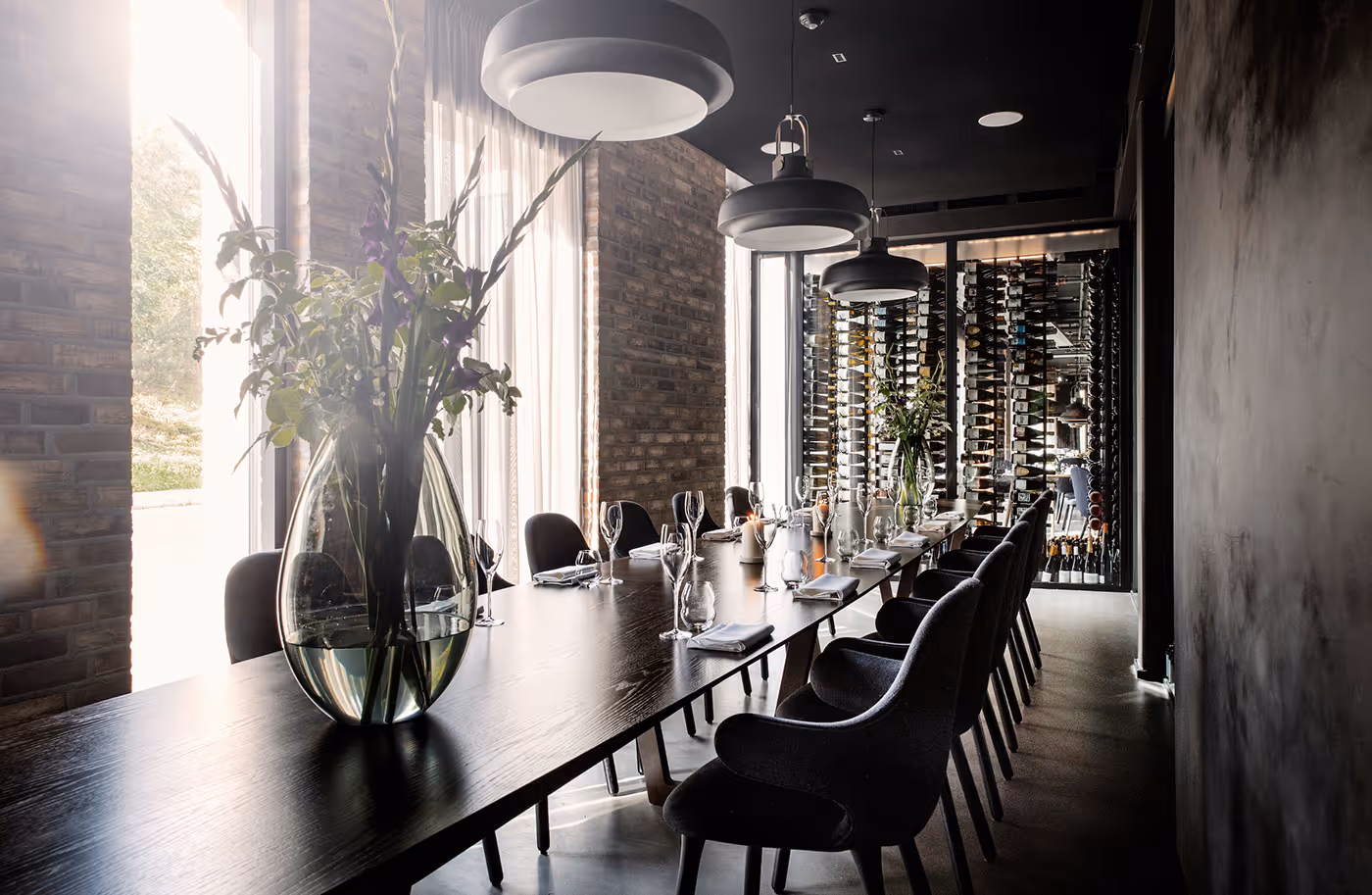 A long set table with chairs in the private dining room at Kontrast, with wine shelves in the background.